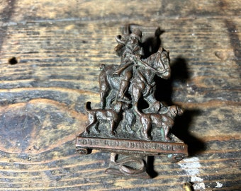 May include: A bronze door knocker depicting a man on horseback with two hounds. The knocker is inscribed with the text "John Peel" and has a scroll design.