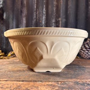 May include: A large, off-white ceramic mixing bowl with a fluted design and a raised rim. The bowl has a textured surface and is slightly angled.