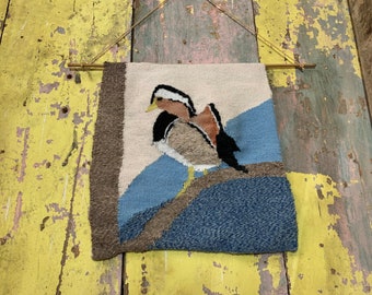 Op de afbeelding: Een geweven wandkleed met een bruine en witte vogel op een blauwe en bruine achtergrond.