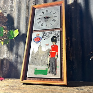 Könnte beinhalten: Eine gerahmte Wanduhr mit einem silbernen Zifferblatt und einem Bild eines rot uniformierten Wächters vor dem Tower of London. Das Bild enthält den Text "Tower of London, The Jewel of London".