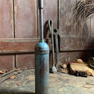 May include: A vintage blue metal grease gun with a long metal nozzle. The gun is rusty and has a gray plastic base.