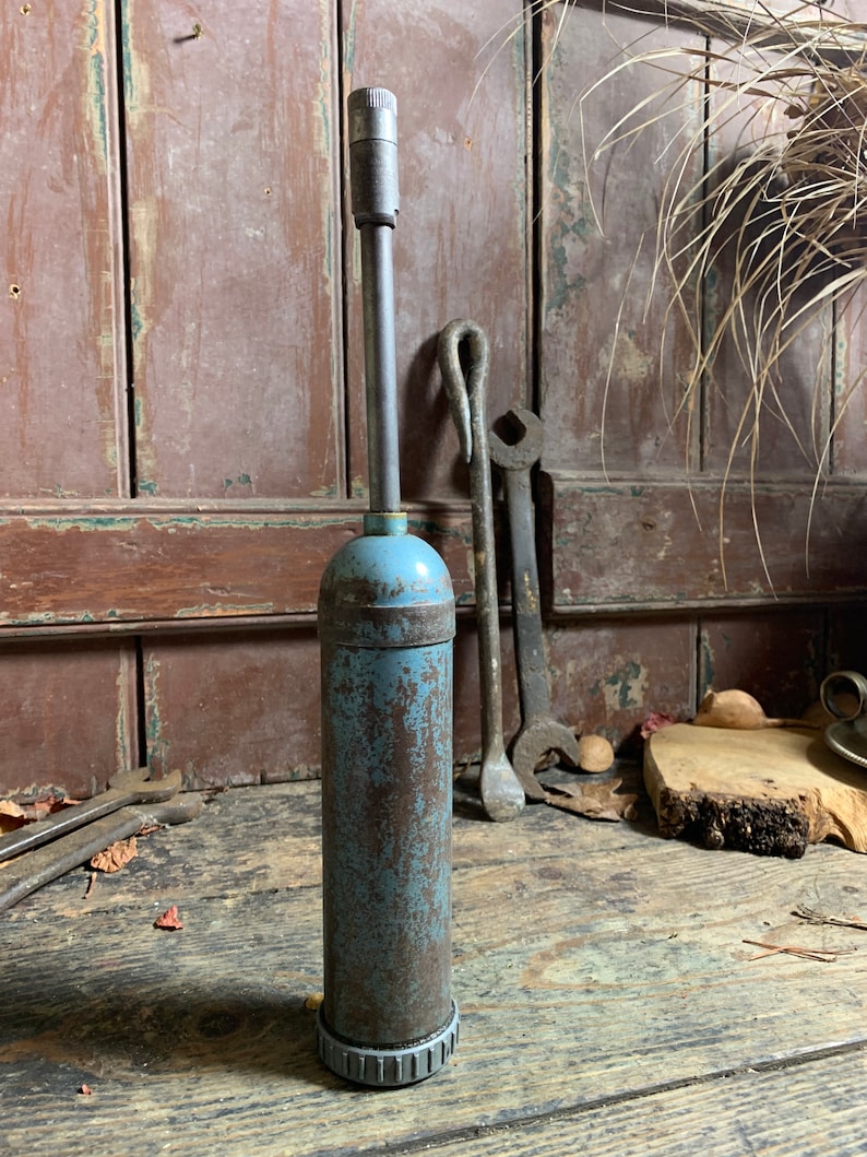 May include: A vintage blue metal grease gun with a long metal nozzle. The gun is rusty and has a gray plastic base.