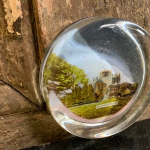 Könnte beinhalten: Ein durchsichtiger Glas-Briefbeschwerer mit einem Vintage-Foto eines Gebäudes und Bäumen. Der Text "BUCKFAST ABBEY" ist am unteren Rand des Bildes sichtbar.