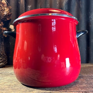 May include: A vibrant red enamel pot with a matching lid and black handles. The pot has a shiny finish and a silver rim. This kitchenware item is suitable for cooking and food preparation.