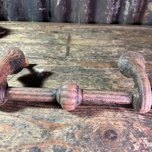 Peut inclure: Une paire de poignées de porte en fonte rouillée avec des détails ornés. Les poignées sont reliées par une longue barre droite avec un bouton décoratif au centre.