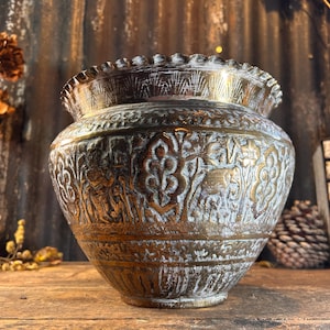 May include: An antique brass planter with an intricate floral design. The planter has a white patina and is in good condition.