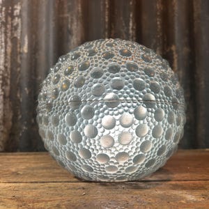 May include: A spherical glass container featuring a textured surface composed of numerous raised circular bumps of varying sizes. The clear glass object has a horizontal seam running through the middle, indicating a two-piece construction.