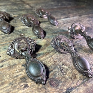 Könnte beinhalten: Satz von acht antiken Bronze-Schubladengriffen mit verzierten Details. Jeder Griff verfügt über einen runden Knopf mit einem dekorativen Ring und einem tropfenförmigen Griff.