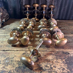 Könnte beinhalten: Eine Sammlung von Vintage-Türknäufen aus Messing mit ovalen Griffen und runden Montageplatten. Jeder Knauf verfügt über einen zentralen Metallstift zur Installation. Das Set enthält mehrere passende Beschläge, die in Reihen angeordnet sind.