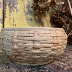 May include: A beige ceramic planter with a woven pattern. The planter has a rounded shape and a slightly textured surface.