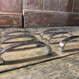 Könnte beinhalten: Acht verchromte Schrankgriffe mit einem geschwungenen, gewölbten Design. Die Griffe sind in zwei Reihen auf einer Holzoberfläche angeordnet.