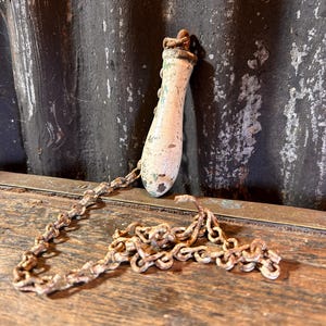 May include: An antique, off-white and gold-toned pull chain with a decorative handle. The chain and handle show signs of age and wear, suggesting a vintage or salvaged item. The chain is made of small, linked metal pieces.
