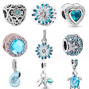 May include: A collection of silver charm beads with blue and white enamel accents. The charms include a heart, a flower, a seashell, a starfish, and a turtle.