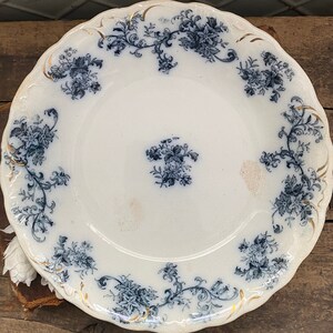 May include: White ceramic plate with a scalloped edge, adorned with blue floral patterns and gold accents. The plate features a central floral design and additional floral arrangements around the rim, creating an elegant aesthetic.