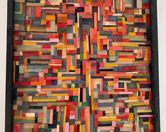 May include: Abstract wooden art piece with a black frame. The artwork is composed of small, rectangular blocks of wood in various colors, including red, orange, yellow, blue, and pink. The arrangement creates a textured, mosaic-like appearance.