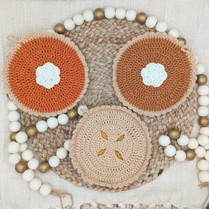 Peut inclure: Trois dessous-de-plat en crochet de différentes couleurs et motifs. Les dessous-de-plat sont ronds et ont un centre blanc avec un motif en crochet. Les dessous-de-plat sont sur un fond tissé avec des perles blanches.