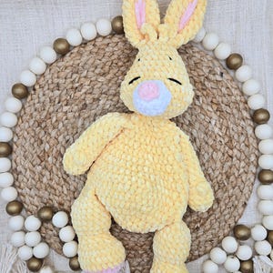 May include: A handmade crochet plush rabbit made from soft yellow yarn. The rabbit features long ears with pink inner accents, a white muzzle, a pink nose, and embroidered closed eyes. The limbs are rounded and the feet have pink details.