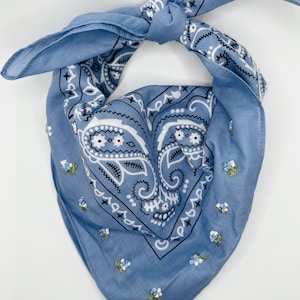 May include: A blue bandana with a white paisley pattern and embroidered blue flowers. The bandana is tied in a knot at the top.