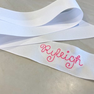 May include: White satin ribbon with the name "Ryleigh" embroidered in pink thread.