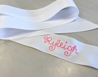 May include: White satin ribbon with the name "Ryleigh" embroidered in pink thread.