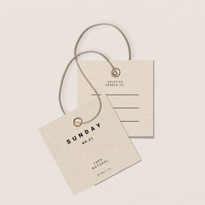 May include: A beige square tag with the text "SUNDAY NO. 21 100% NATURAL 20 ML/FL" and a gold metal ring. A smaller beige square tag with the text "SOLSTICE CANDLE CO." is attached to the larger tag with a brown string.