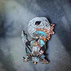 May include: Enamel pin featuring a character with a blue cap and tunic, holding a sword, with a skull-like mask behind him. The pin has a black, white, blue, orange, and gold color scheme. The word "Final" is written on the bottom.