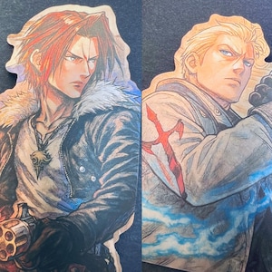 Puede incluir: Dos pegatinas de personajes troqueladas. Una presenta a un hombre con cabello rojo, una chaqueta forrada de piel y un colgante. La otra representa a un hombre con cabello rubio, una chaqueta blanca y un diseño de espada roja. Estilo ilustrado.