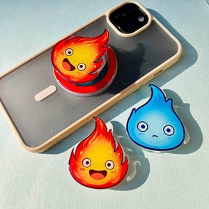 May include: A clear phone case with a red, orange, and yellow fire-themed pop socket and two matching acrylic charms. One charm is a blue flame with a sad face. The other is a happy fire.