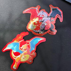 May include: Two holographic stickers featuring the Pokemon characters Charizard and Blastoise. Charizard is red and orange with black wings and a fiery tail. Blastoise is blue and gray with blue wings and water cannons on its back.
