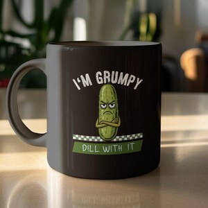 May include: Black ceramic mug with the text "I'M GRUMPY" above a cartoon pickle with crossed arms. Below the pickle is the text "DILL WITH IT" on a green and white checkered banner. The mug has a curved handle.