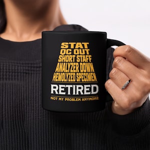 May include: Black ceramic mug with the words "STAT OC OUT SHORT STAFF ANALYZER DOWN HEMOLYZED SPECIMEN RETIRED NOT MY PROBLEM ANYMORE" in yellow and white lettering. The mug is held by a person.