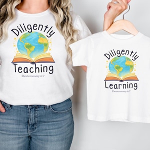 May include: White t-shirts with matching designs. One shirt says "Diligently Teaching" with a globe and open book graphic. The other says "Diligently Learning" with the same graphic. Both shirts have the Bible verse Deuteronomy 6:7.