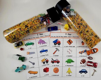 Può includere: Due bottiglie sensoriali trasparenti riempite di riso giallo e arancione, con tappi neri. Le bottiglie sono accanto a carte di gioco "I Spy" con giocattoli in miniatura. Le carte hanno illustrazioni di un'auto, un camion e altri oggetti.