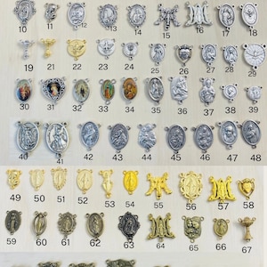 May include: A collection of 74 silver and gold religious medallions, charms, and pendants. The medallions feature various religious figures and symbols, including the Virgin Mary, Jesus Christ, and the Holy Spirit. The medallions are arranged in rows and columns on a wooden surface.
