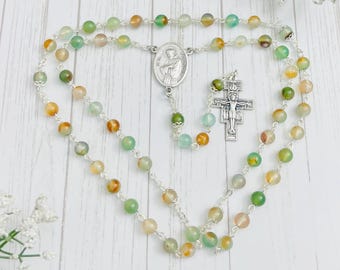 May include: A green and brown agate stone rosary with a silver crucifix and a silver medal of Saint Francis of Assisi.