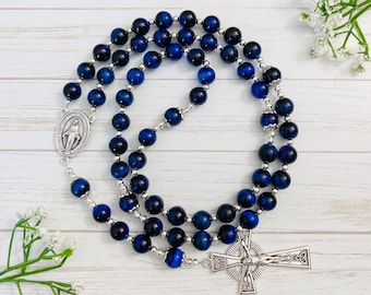 Può includere: Rosario blu e argento con una croce d'argento e un ciondolo d'argento della Vergine Maria. Le perle sono in occhio di tigre blu.