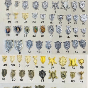 May include: A collection of 74 silver and gold religious medallions, charms, and pendants. The medallions feature various religious figures and symbols, including the Virgin Mary, Jesus Christ, and the Holy Spirit. The medallions are arranged in rows and columns on a wooden surface.