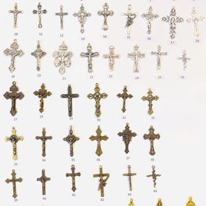 May include: A collection of 52 silver, bronze, and gold cross charms. The charms are arranged in rows on a white background. Each charm is numbered from 1 to 52.