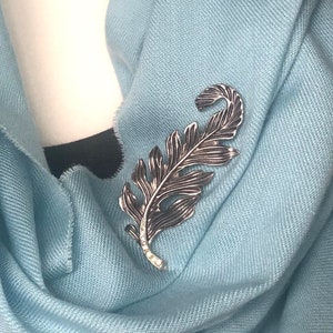 May include: A light blue scarf with a silver feather brooch.