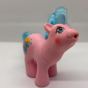 May include: A pink toy pony with blue hair and a blue tail. The pony has a yellow and blue design on its side. The pony has a blush on its cheeks and is looking up.