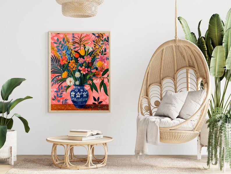 May include: A framed painting of a blue and white vase filled with a colorful bouquet of flowers. The vase is sitting on a pink background with a floral pattern. The painting is hanging on a white wall.