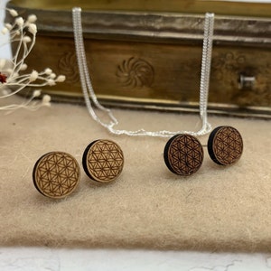 Könnte beinhalten: Drei Holzohrringe mit einem Lebensblume-Design. Die Ohrringe sind braun und haben eine schwarze Rückseite. Die Ohrringe liegen auf einer hellbraunen Oberfläche.