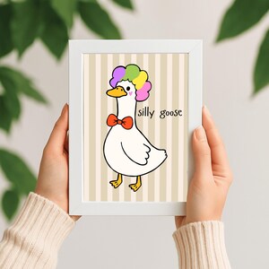 Peut inclure: Illustration encadrée d'une oie de dessin animé avec une perruque colorée et un nœud papillon rouge. L'oie blanche a des pieds jaunes et un bec jaune. Le texte "silly goose" est écrit sur l'image.