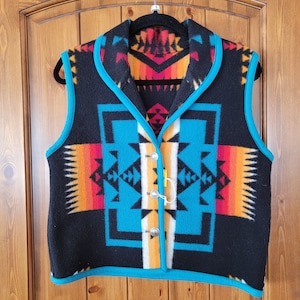 Puede incluir: Un chaleco de vellón negro con ribete turquesa y un patrón geométrico de inspiración suroeste en tonos naranja, rojo, blanco y azul.