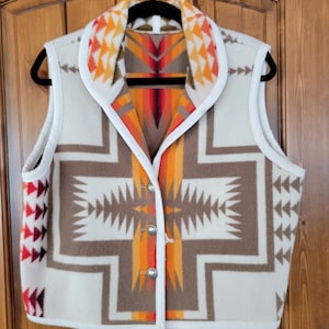 Puede incluir: Un chaleco blanco con un patrón geométrico marrón, naranja y rojo. El chaleco tiene un cuello blanco y un cierre de botón.