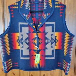 Puede incluir: Chaleco reversible azul marino con un patrón geométrico en tonos de rojo, naranja, amarillo y marrón. El chaleco tiene cuello y cierre de botón. La etiqueta dice "Reversible Talla Grande".