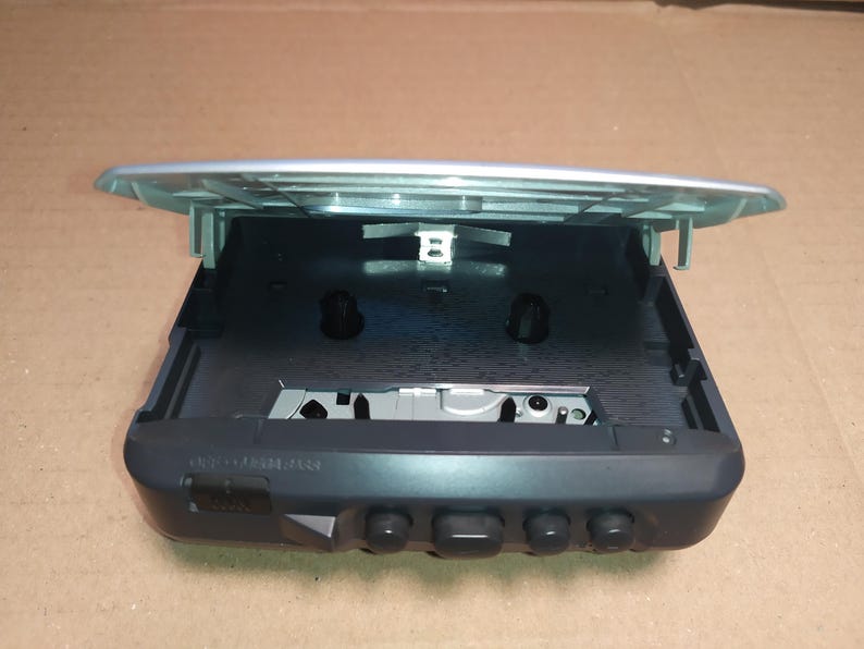 May include: A silver and black cassette player with the top open, revealing the cassette tape slot. The player has several buttons on the front.