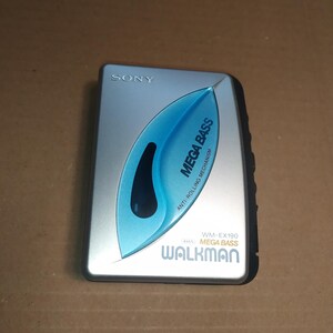 May include: A silver Sony Walkman cassette player with a blue "Mega Bass" logo and the text "Anti-Rolling Mechanism". The player has a black button on the right side.