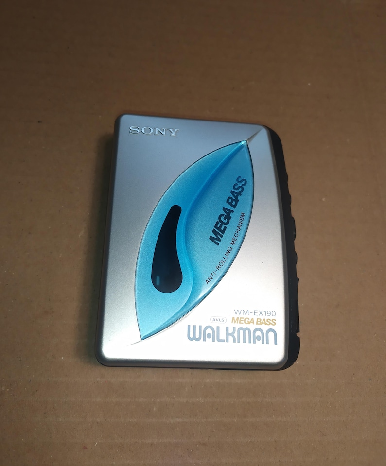 May include: A silver Sony Walkman cassette player with a blue "Mega Bass" logo and the text "Anti-Rolling Mechanism". The player has a black button on the right side.