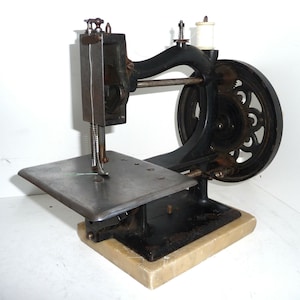 Pode incluir: Uma máquina de costura vintage preta com uma base de mármore branco. A máquina tem uma roda grande e uma agulha enfiada com fio verde.